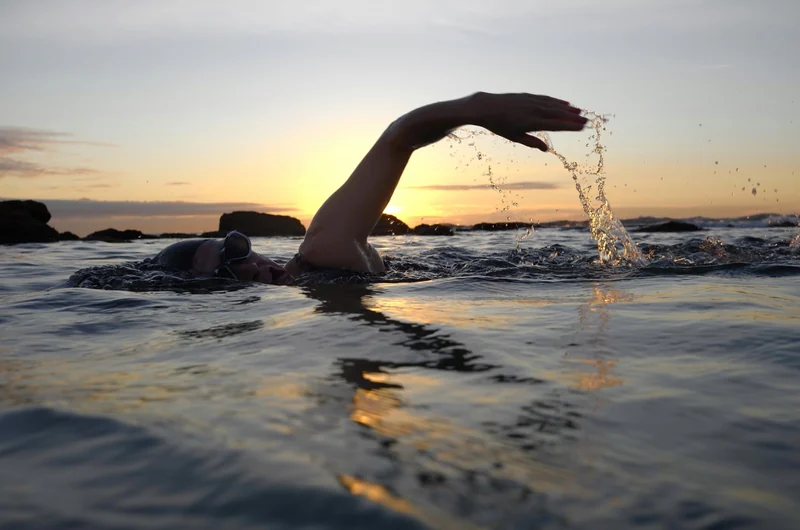 A swimmer in open water at sunrise.