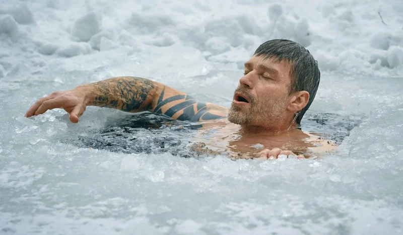A man swims in a frozen lake between ice and snow.