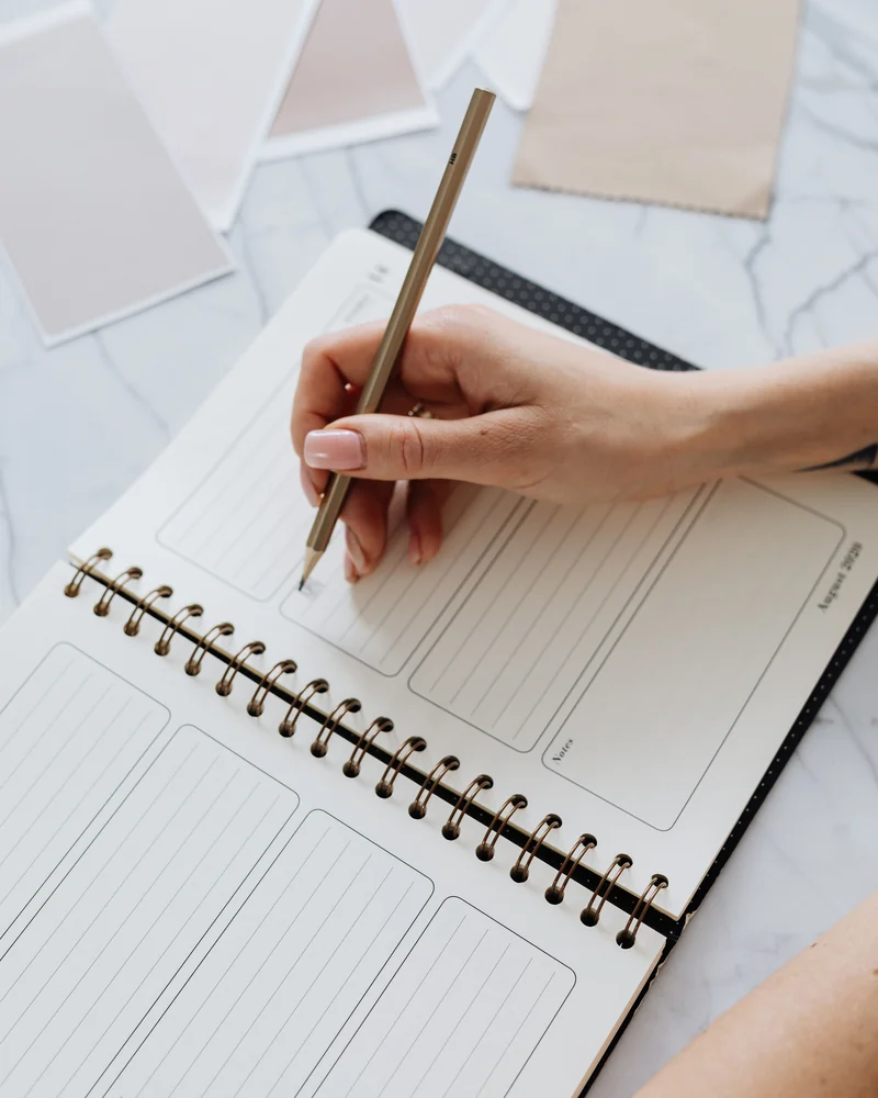 A hand writes in a weekly planner.