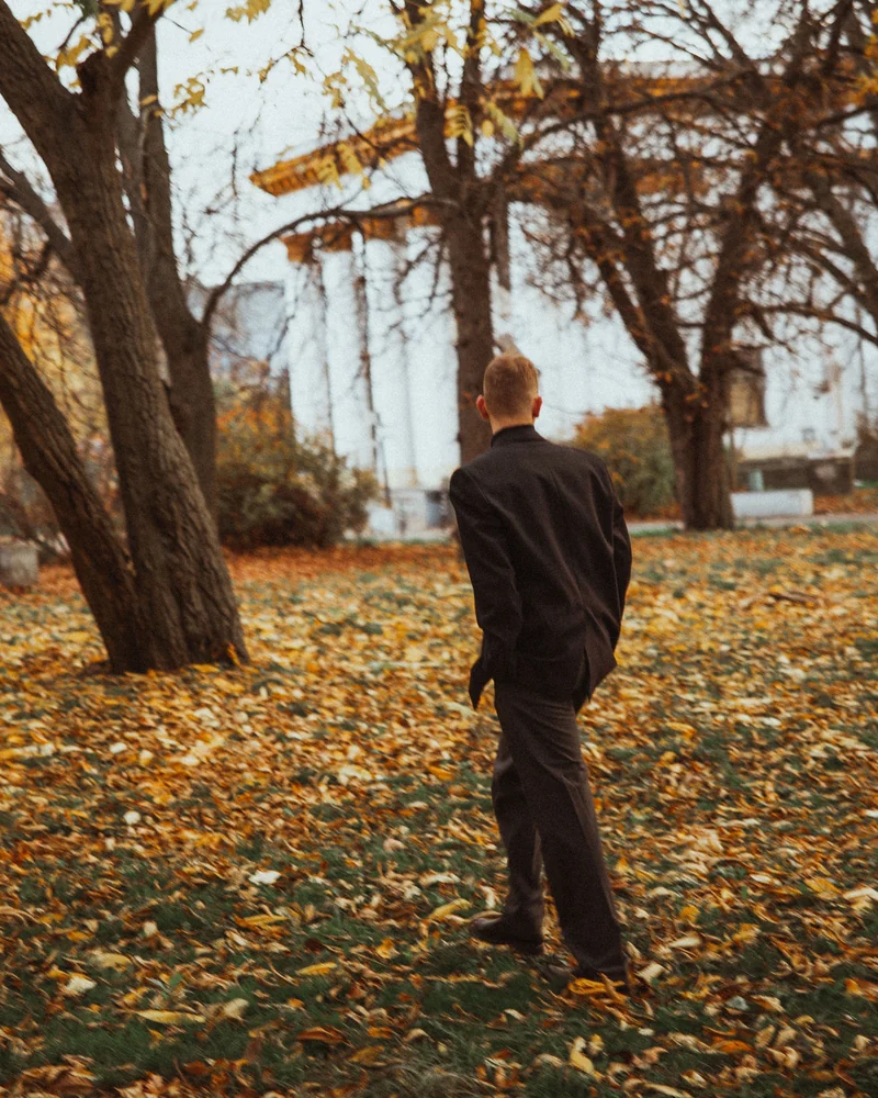 A man in a dark coat walks through an autumn park.