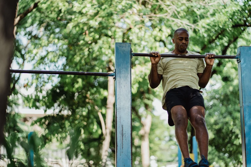 A man does pull-ups on a bar in a park.