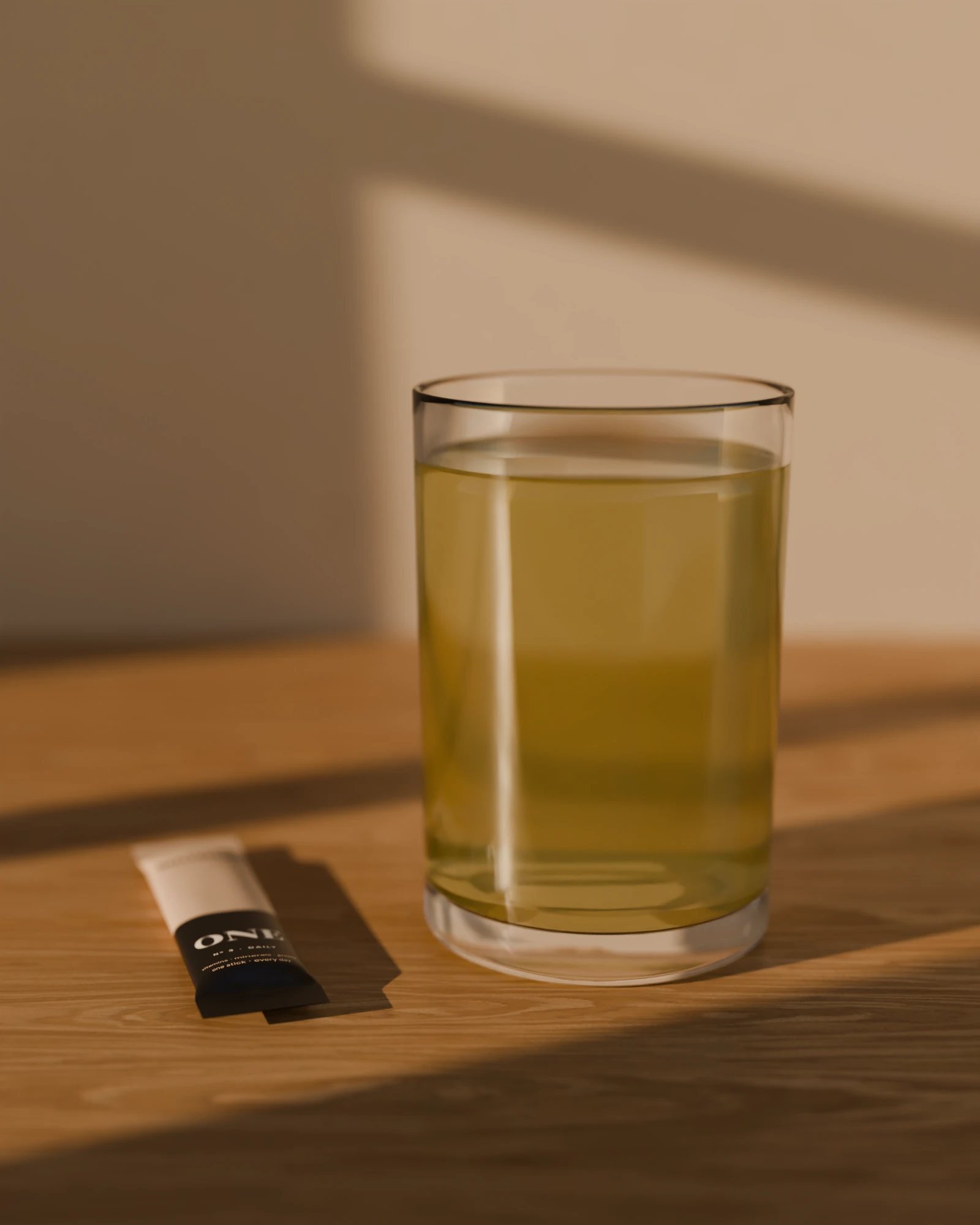 A glass of ONE in 500 ml of water beside a stick, in morning light.